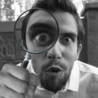A man looking through a magnifying glass at the viewer