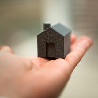 Person holding a small model of a house in their outstretched palm.