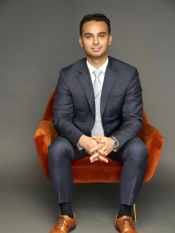 Arya Channaveeraiah, wearing a suit, sitting in a red chair